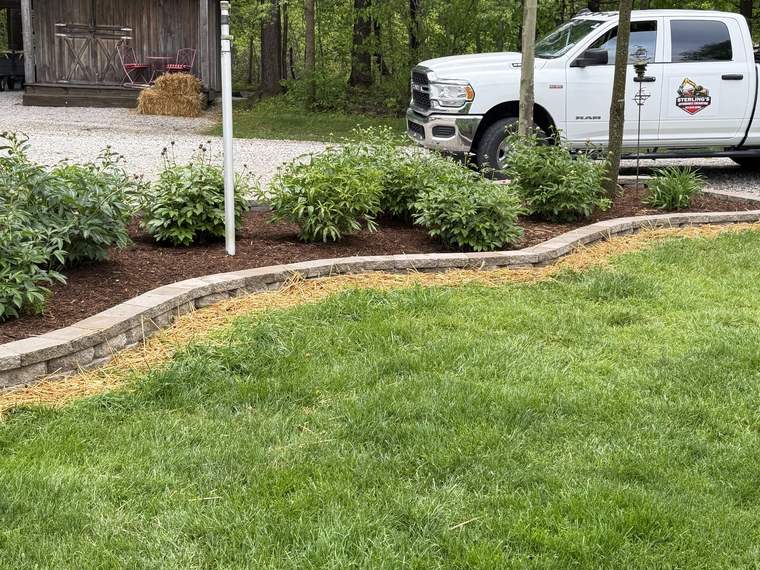Low block retaining wall shaping a front bed in front of an outbuilding