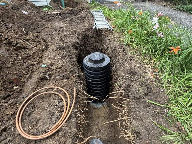 Catch basin riser set in an open excavation in a landscaped bed