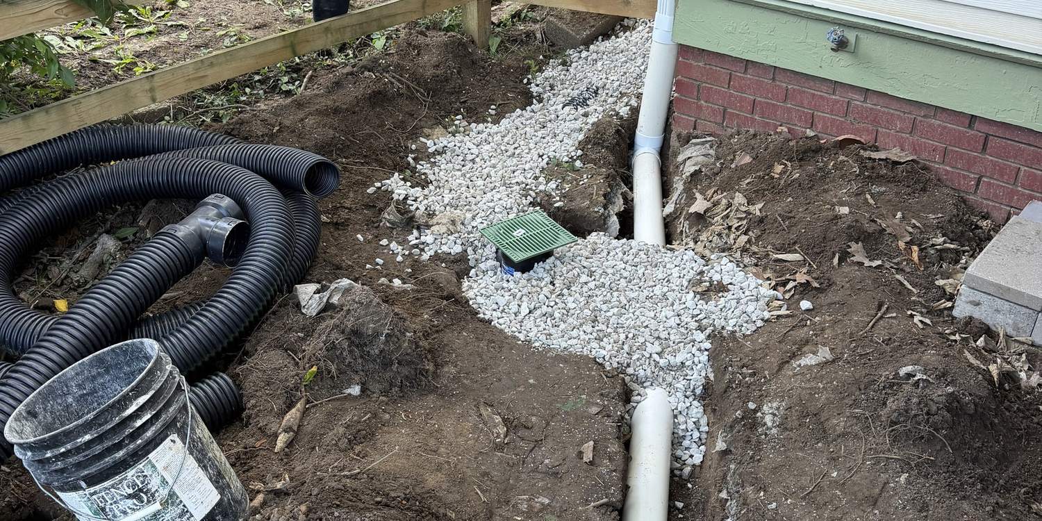 Buried downspout drainage line run in gravel along the side of a house