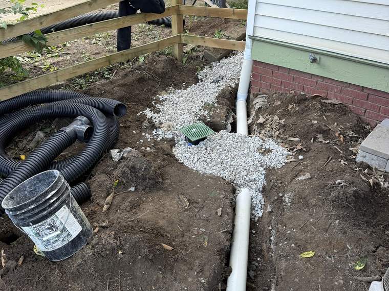 Buried downspout drainage line run in gravel along the side of a house