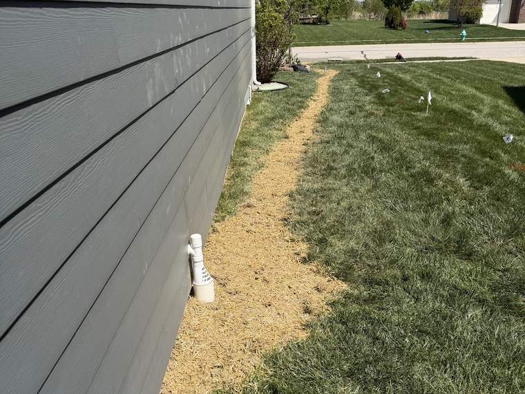 Gravel drainage line running along a house wall with a cleanout riser set flush