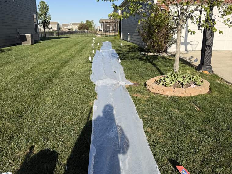 Long drainage trench opened across a front lawn with the spoil laid on plastic