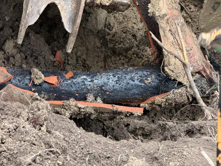 Existing utility line carefully exposed by hand under an excavator bucket