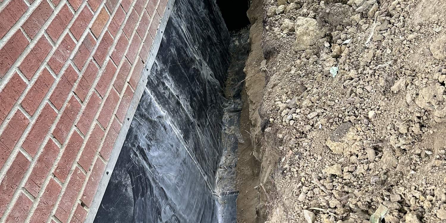 Waterproofing membrane applied to an exposed brick foundation wall in an open trench