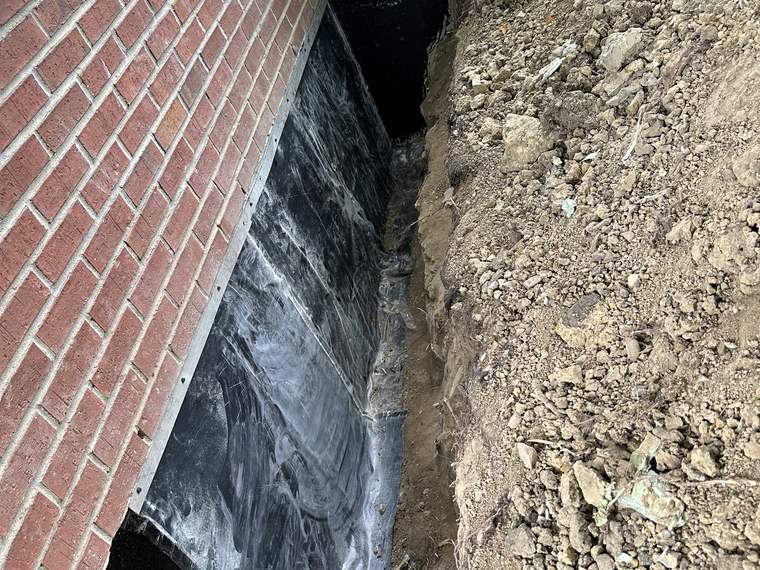 Waterproofing membrane applied to an exposed brick foundation wall in an open trench