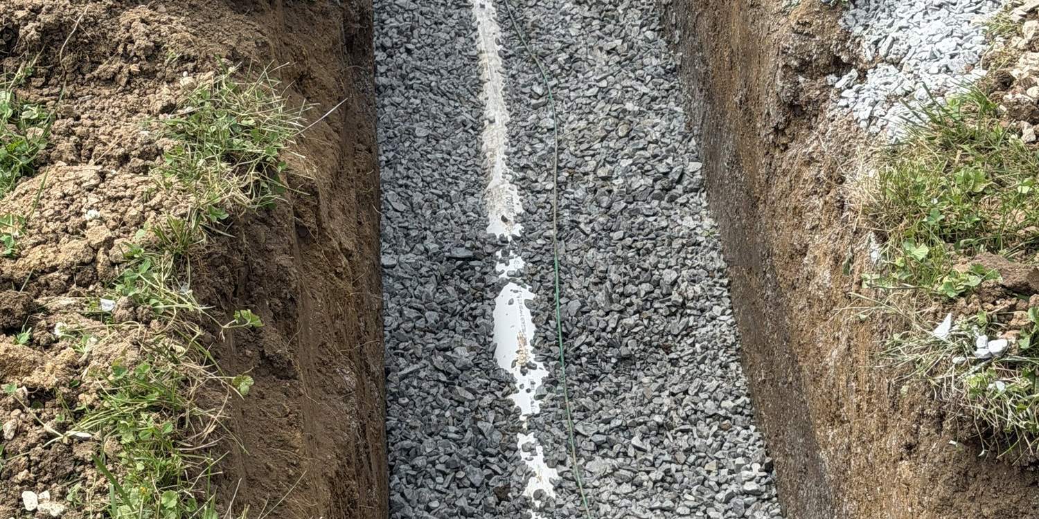 Perforated French drain pipe bedded in washed stone in an open trench