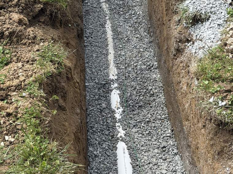 Perforated French drain pipe bedded in washed stone in an open trench