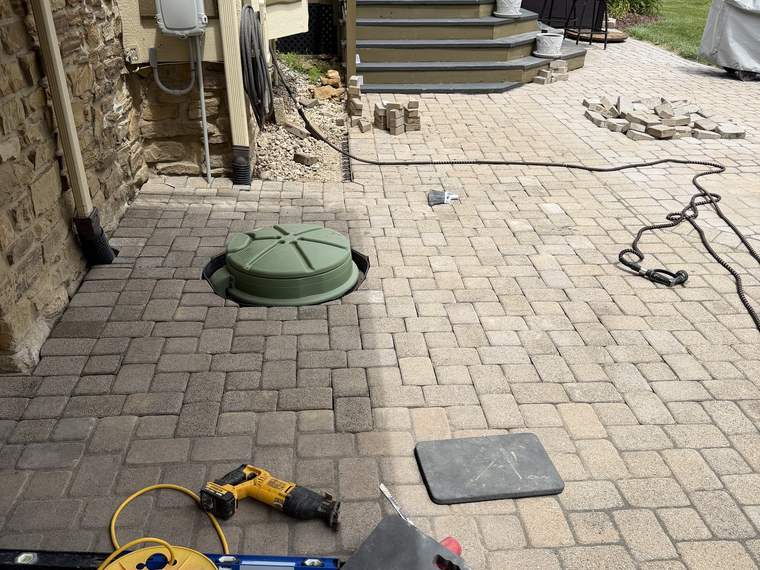Paver patio lifted for access to a lid and buried line underneath