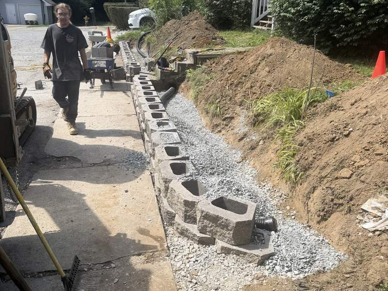Retaining wall under construction with washed stone backfill going in behind it