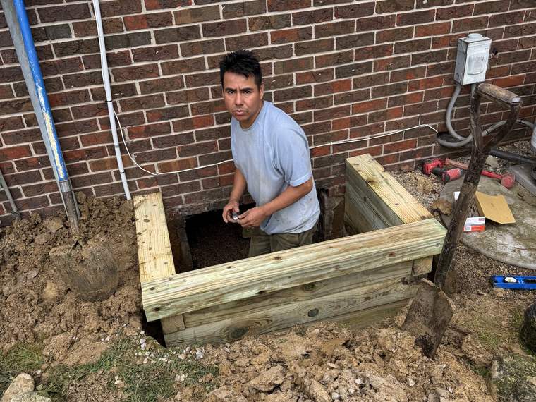 Worker in a shored excavation for utility work beside a brick home