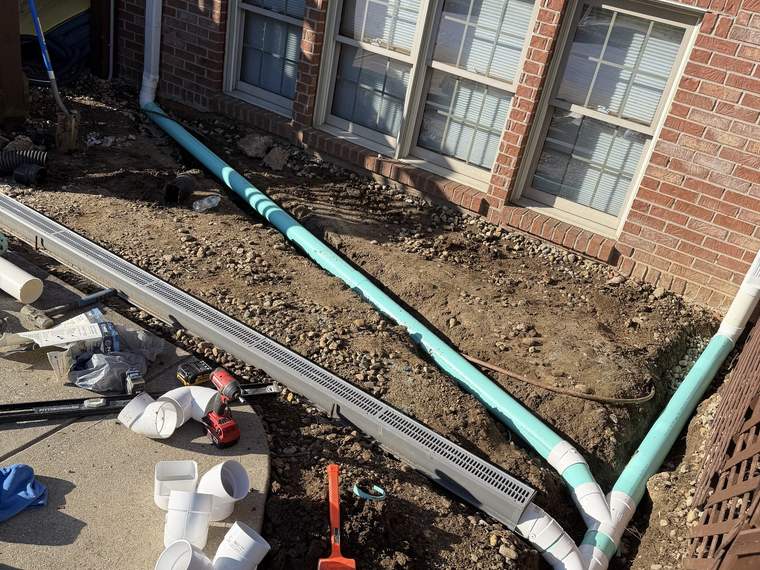 Storm drainage pipe being tied in along the foundation of a brick home